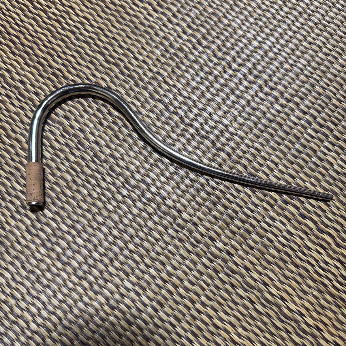 Metal bassoon bocal (mouthpiece) with a cork tenon lying on a woven surface.