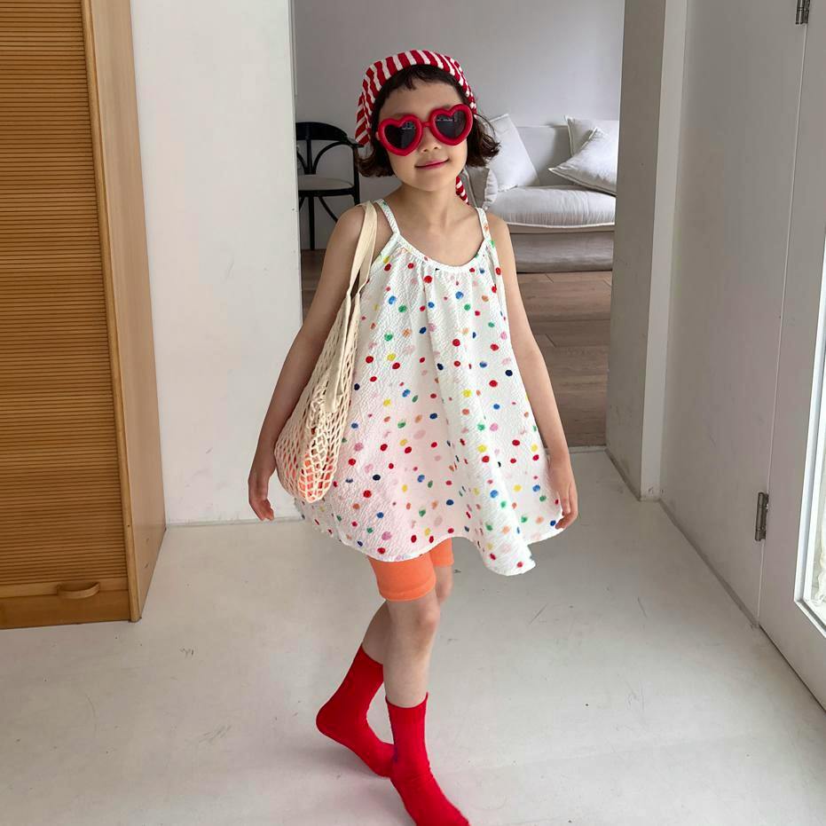 White cotton candy one-piece dress with multicolored polka dots shown on a model wearing red socks and holding a net bag.