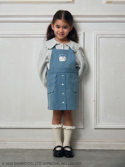 A model wearing a Hello Kitty 2-way jumper skirt over a long-sleeve blouse, standing against a white paneled wall.