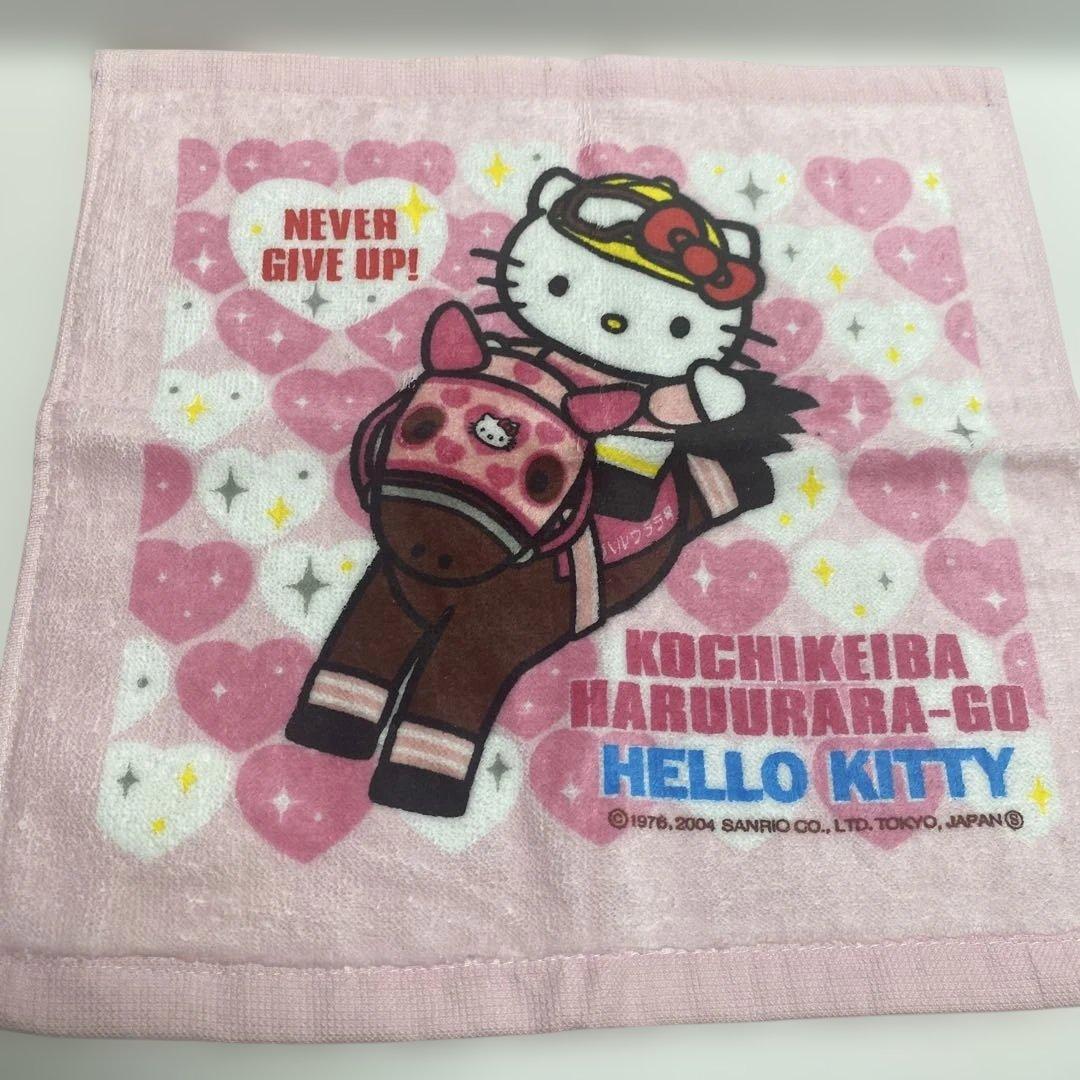 Pink cotton Hello Kitty handkerchief showing Hello Kitty riding a horse, surrounded by hearts and text reading "NEVER GIVE UP!" and "HELLO KITTY."