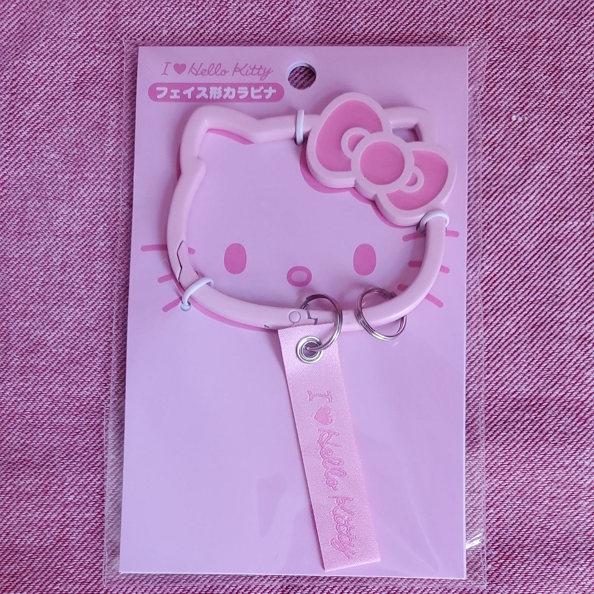 Pink Hello Kitty face-shaped carabiner with a pink tag on a pink backing card inside sealed plastic packaging.
