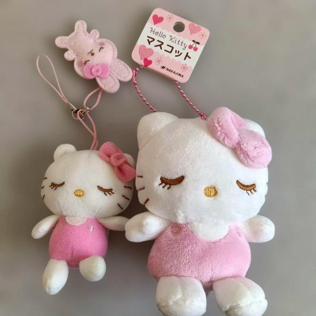 Two Hello Kitty mascot plush toys in white and pink, one larger and one smaller, attached to hanging straps with a product tag.