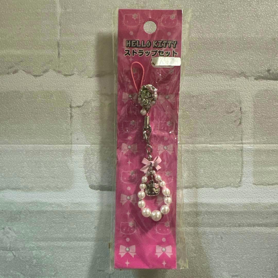 Packaged Hello Kitty pearl-style strap bag charm displayed on a pink bow-pattern backing in plastic packaging.