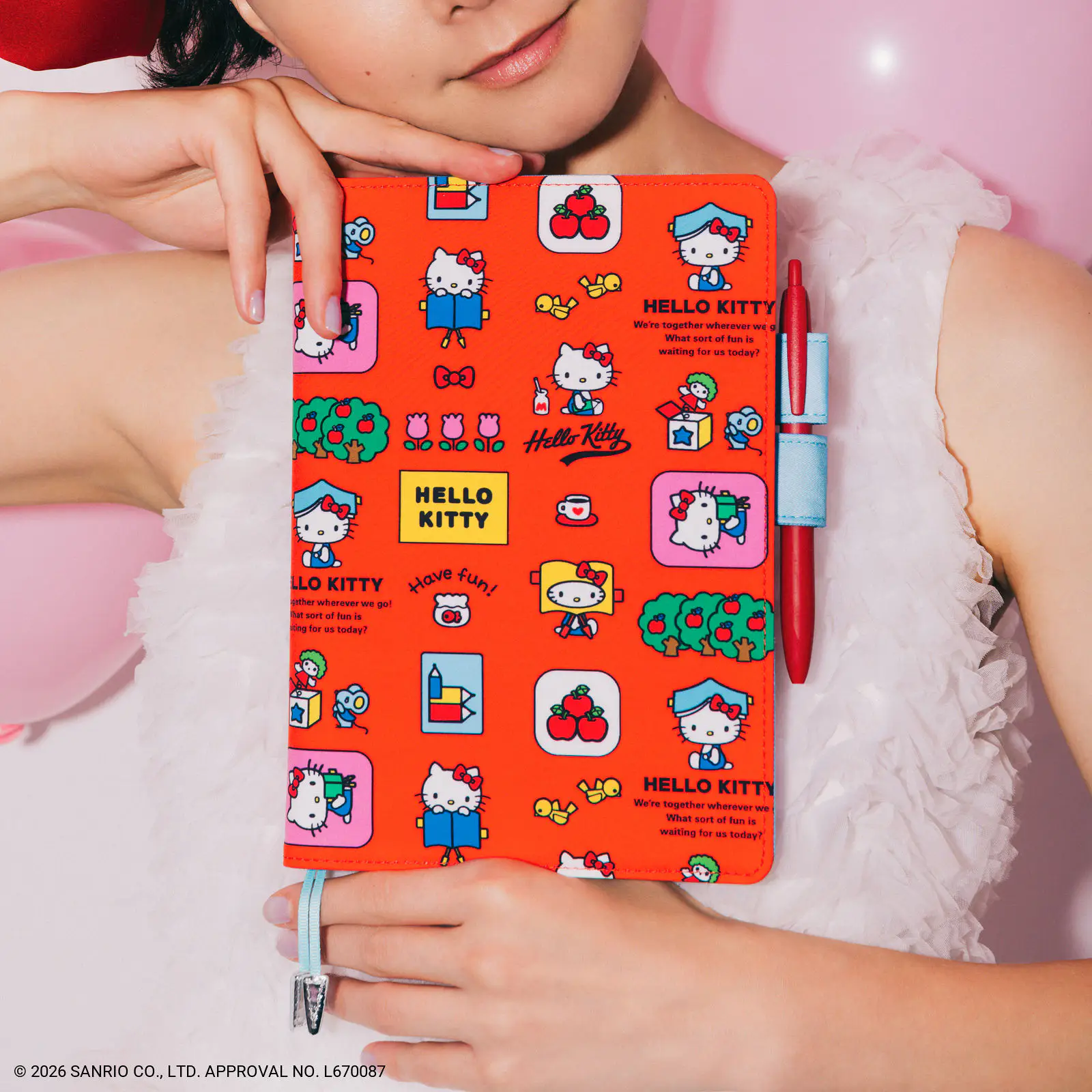 A person holds a red Hello Kitty A5 cousin-size polyester book cover with a cartoon character pattern and a pen attached.
