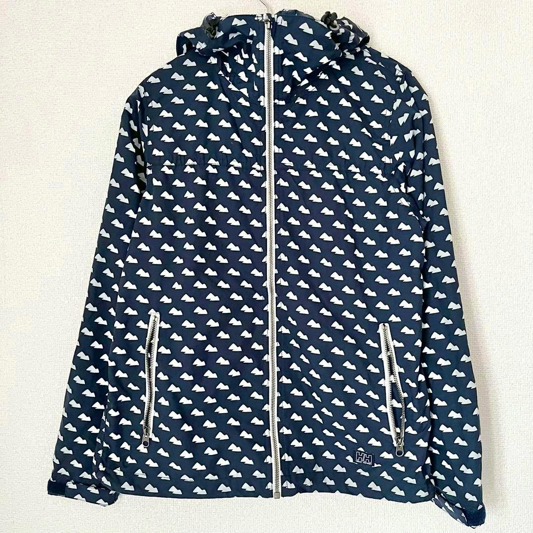 Front view of a Helly Hansen women's jacket (nylon, knitted) hanging on a wall; navy with white repeating cloud-like pattern, center zipper and zippered pockets.