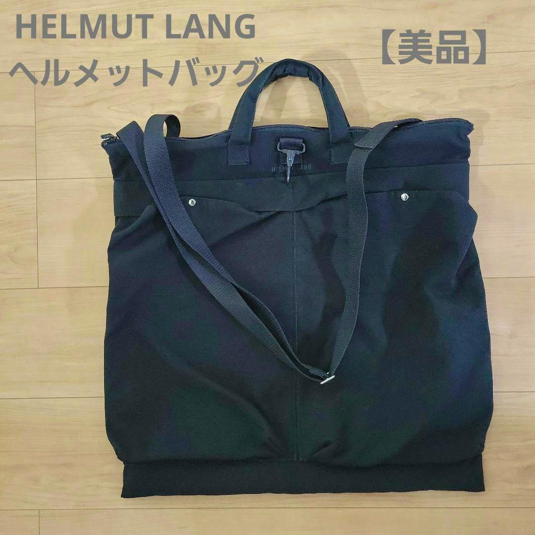 Black Helmut Lang canvas helmet bag with shoulder strap laid flat on a wooden floor, with brand text overlaid at the top.