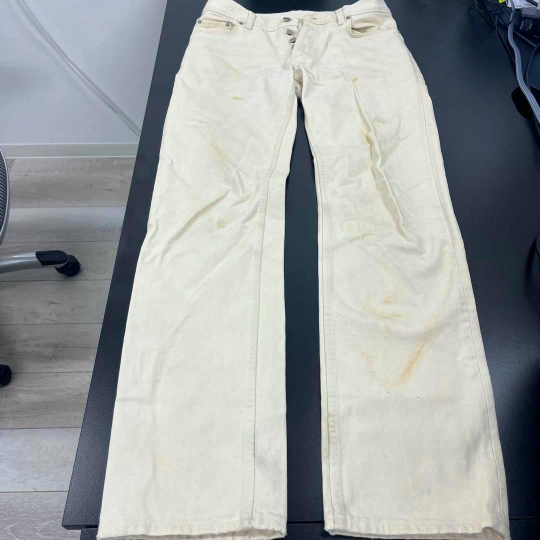 White men's jeans laid flat on a dark surface showing full length with visible discoloration and stains.