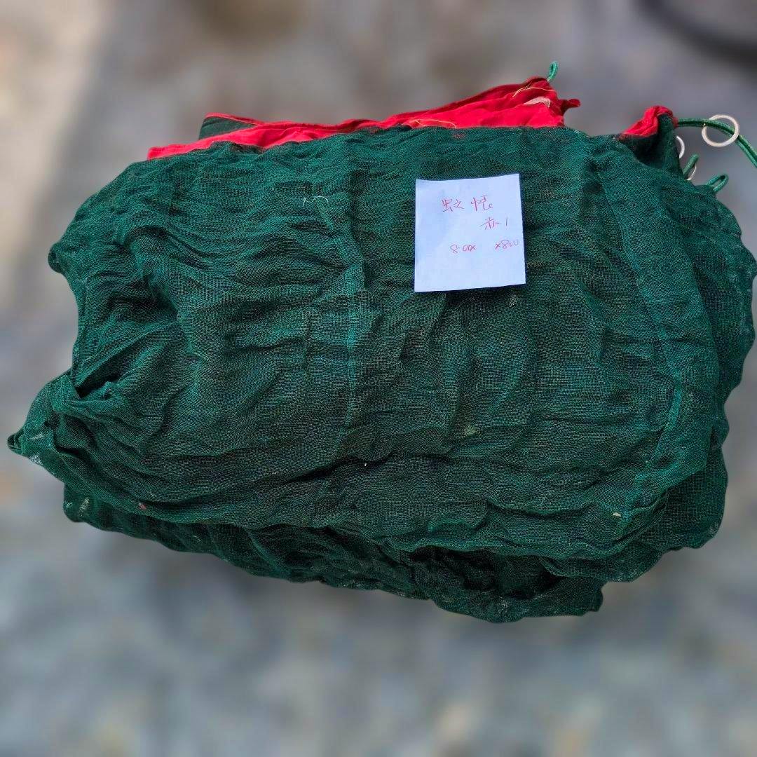 A folded green mosquito net with visible red lining and a small handwritten note placed on top.