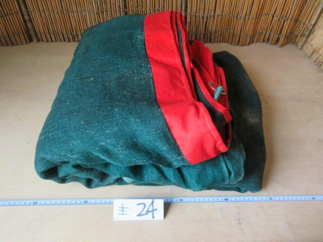 Folded green hemp mosquito net with a red border on a table, with a measuring tape and a small paper tag labeled '主 24'.