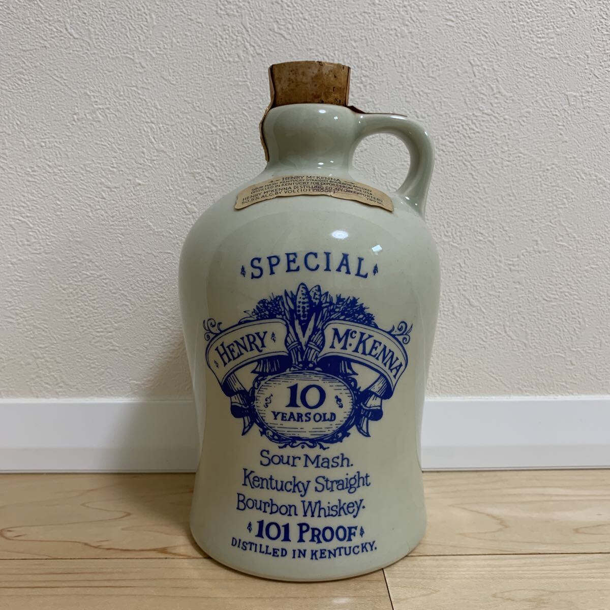 Ceramic Henry McKenna 10‑year 101 proof bourbon bottle with handle, cork, and blue printed label visible.