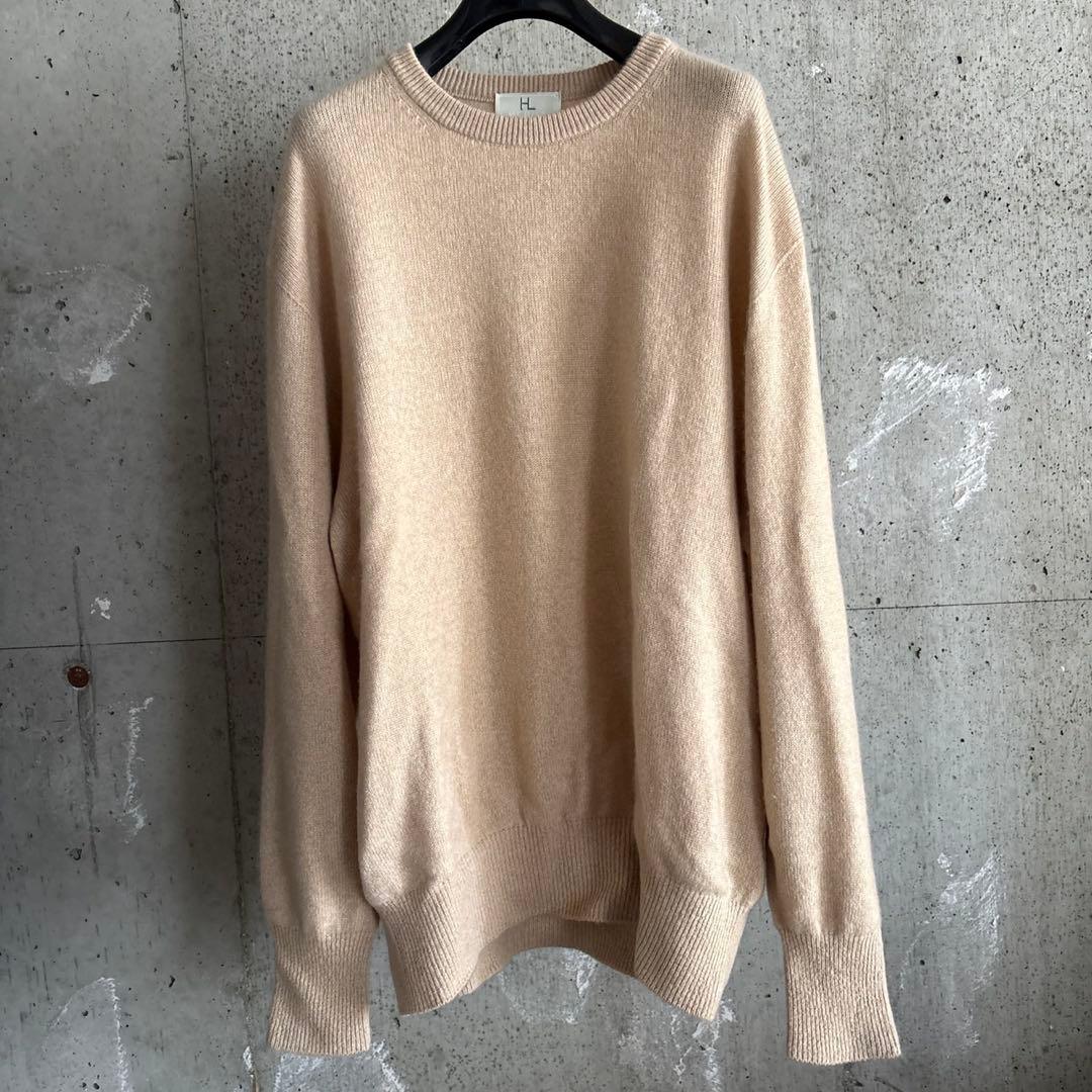 A beige cashmere sweater hanging on a black hanger against a concrete wall.