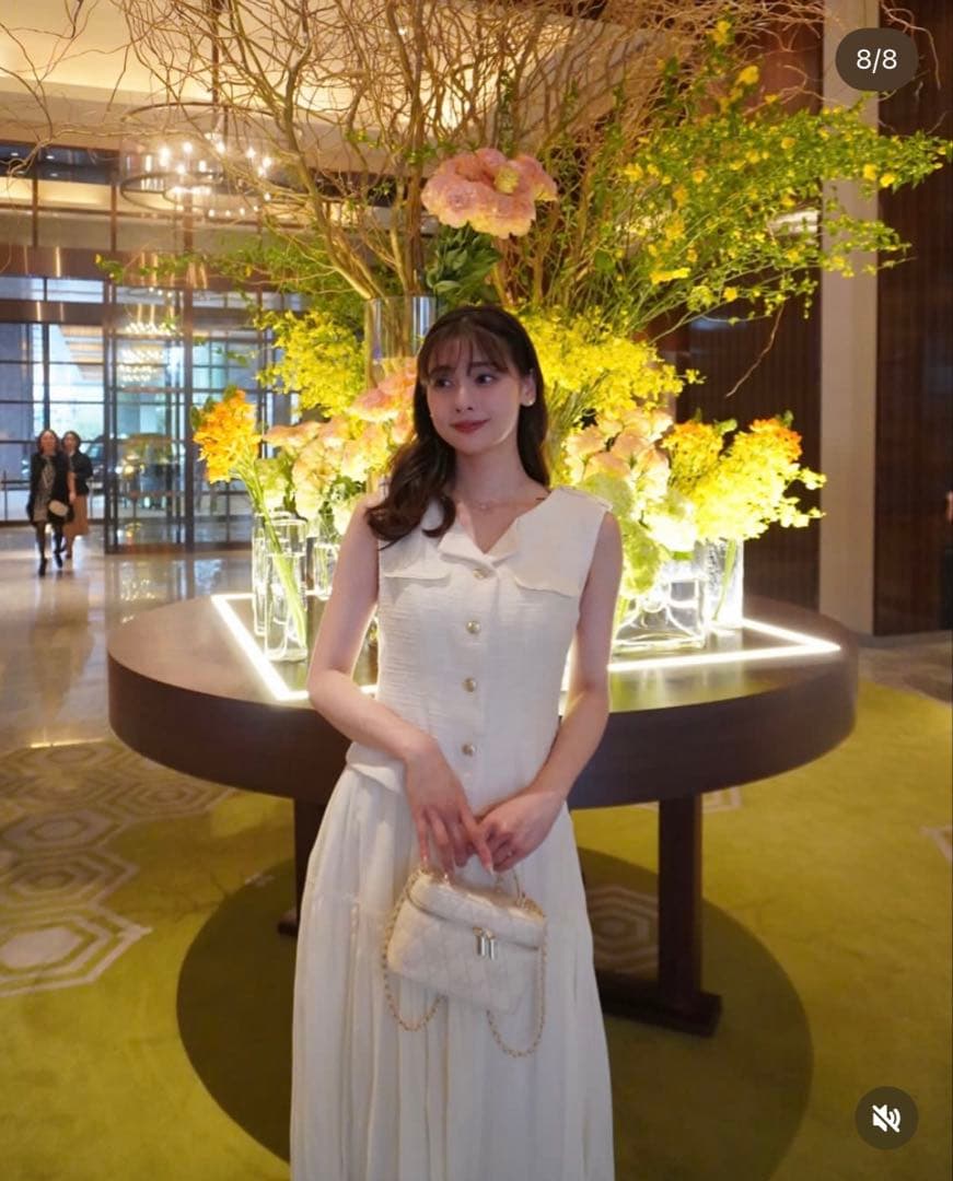 Model wearing the white Herlipto Emma Tweed Docking Dress standing indoors in front of a floral display.