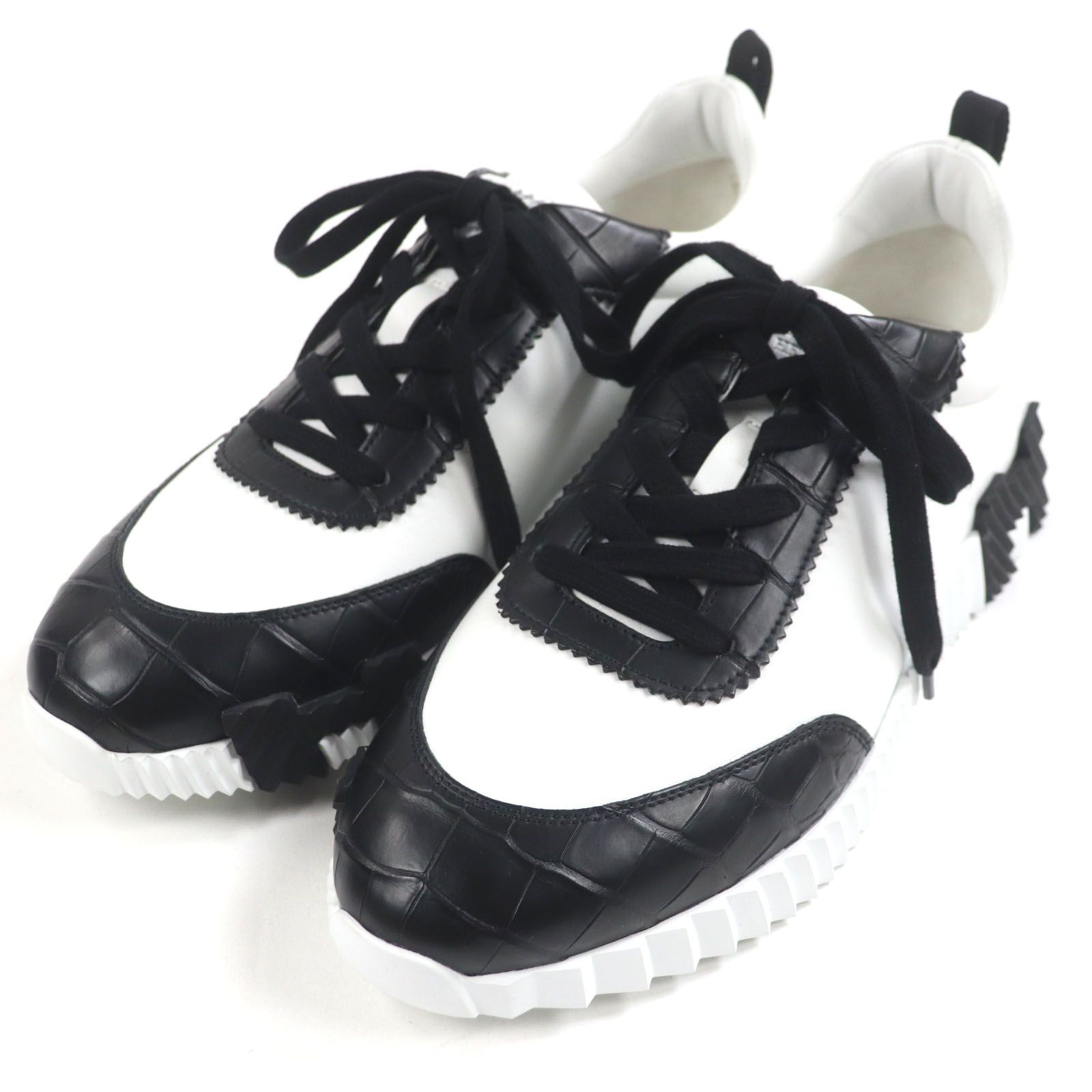 Pair of white and black Hermes men's leather sneakers with crocodile-pattern detailing shown from an angled top view.