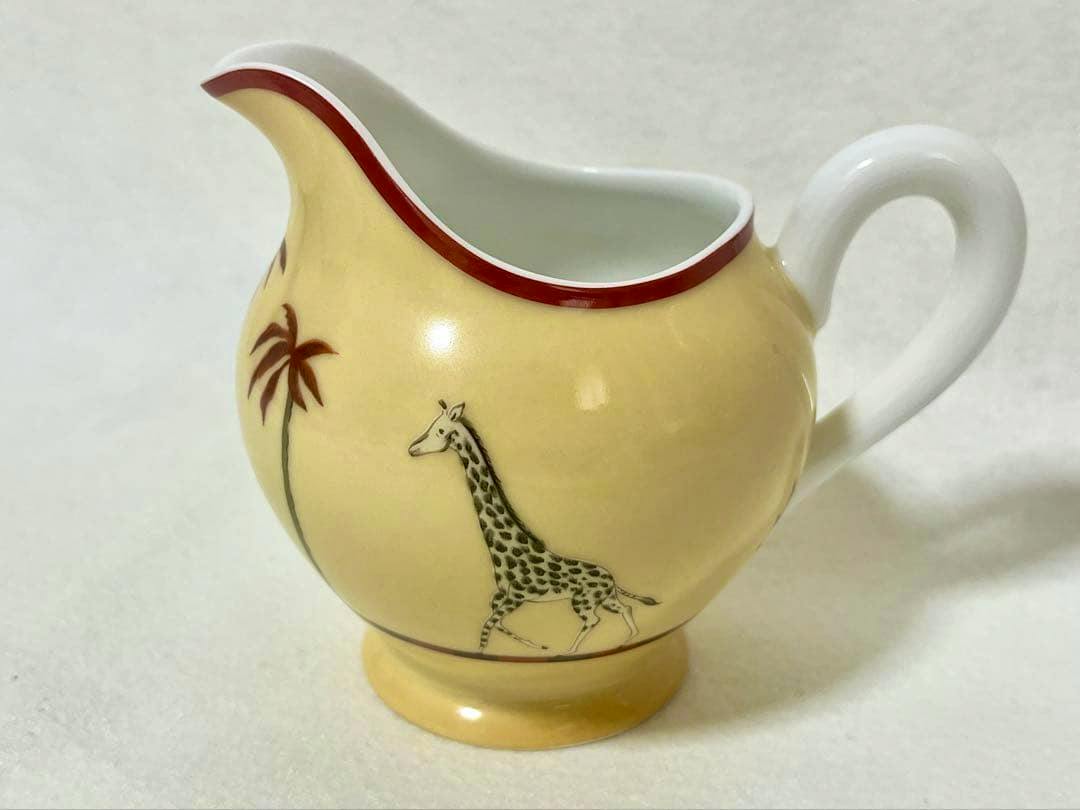 Yellow Hermès creamer showing a giraffe and palm tree motif, white handle, and red rim.