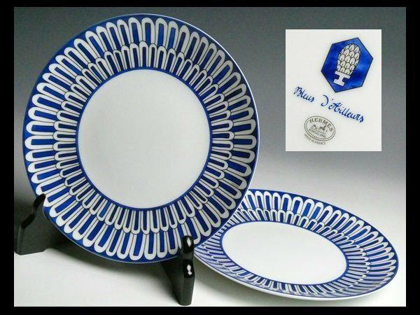 Two Hermès blue-patterned ceramic plates (pair), one displayed upright on a stand and one lying flat.