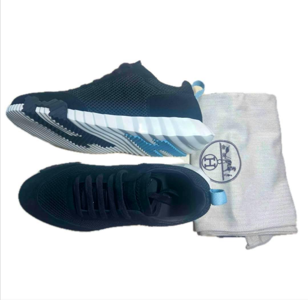 Top and side views of HERMES women's Bouncing sneakers in black and blue shown next to a dust bag.