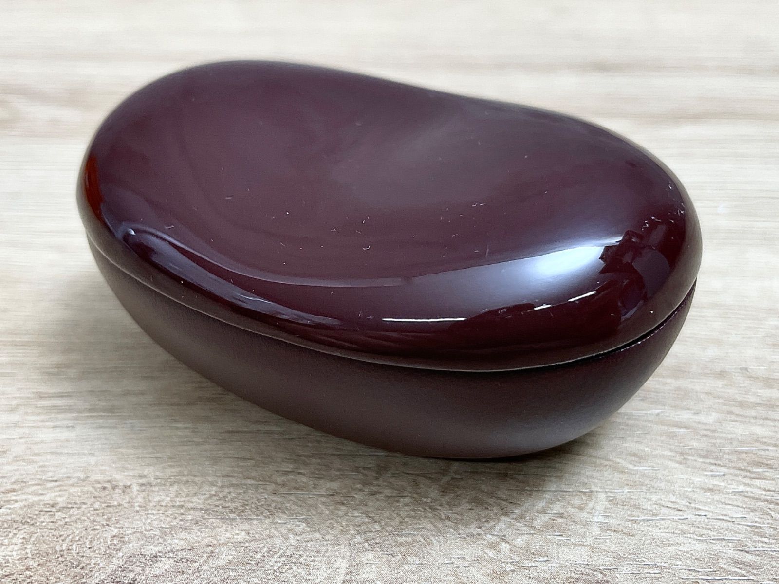 A brown bean-shaped wooden case resting on a light wood surface.