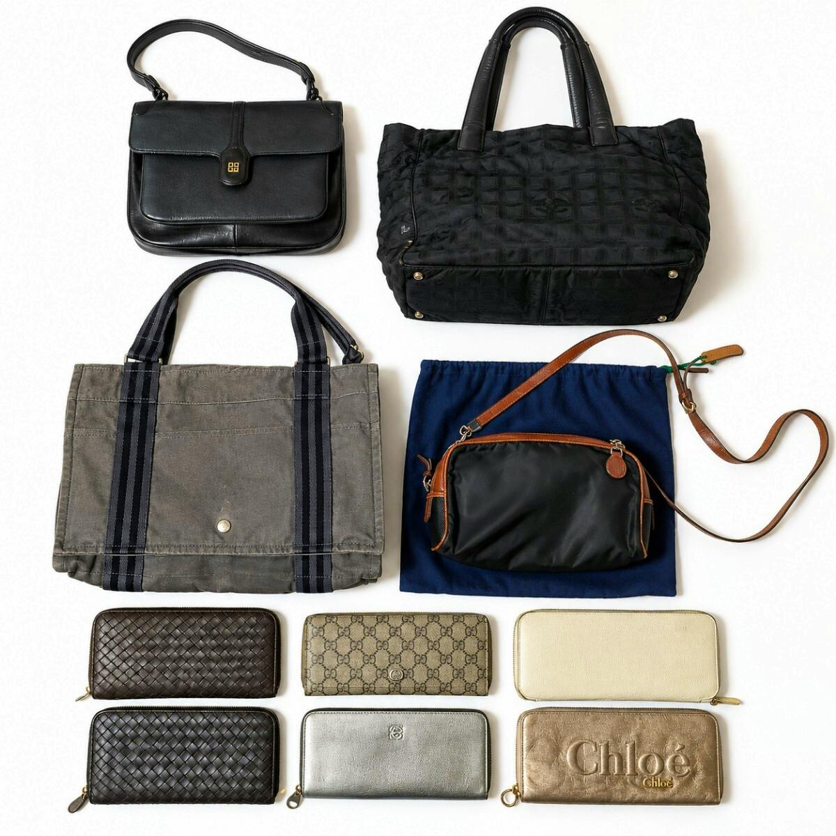 Top-down photo of multiple high-brand bags and wallets arranged on a white background, showing several handbags, a canvas tote, and multiple zip wallets.