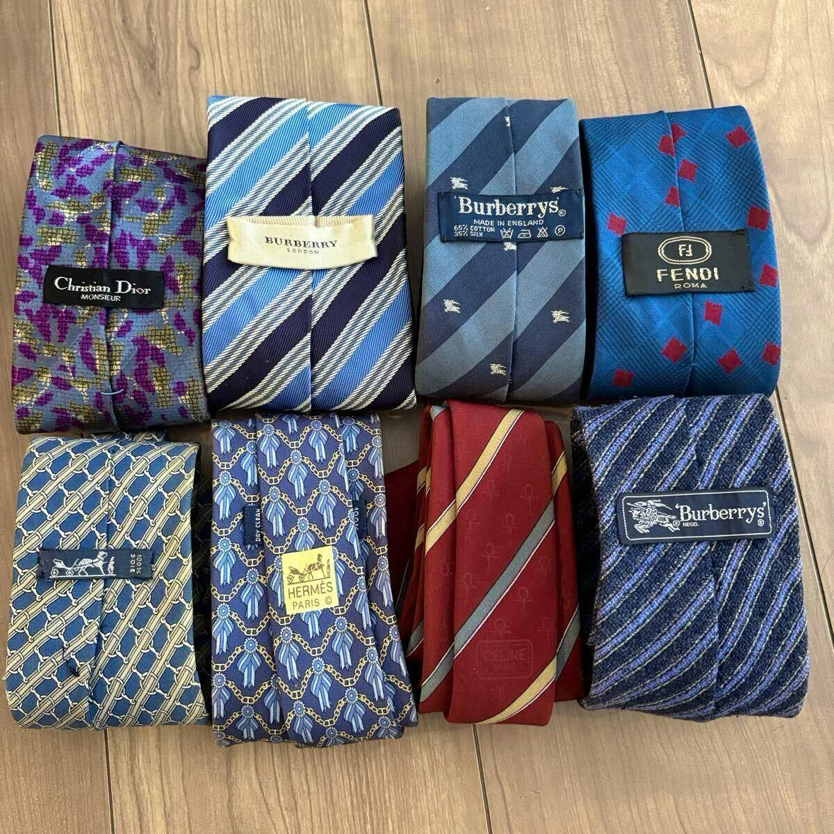 Eight folded neckties with visible designer labels (Christian Dior, Burberry, Burberrys, Fendi, Hermès, Celine) arranged on a wooden surface.