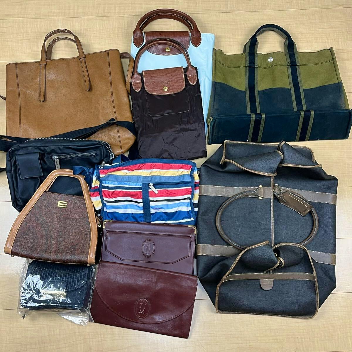 Eleven assorted branded bags arranged on a wooden floor, showing various totes, canvas and leather styles.