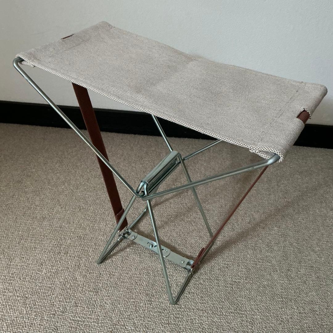 Beige fabric folding chair with a metal frame and brown straps, shown unfolded on carpet.
