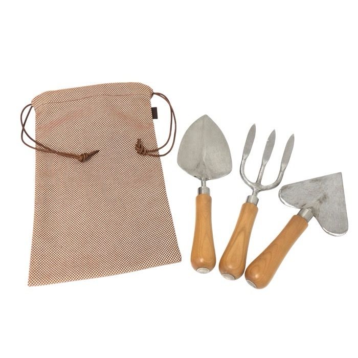 Three metal gardening tools (scoop, fork, trowel) with wooden handles next to a patterned drawstring bag.