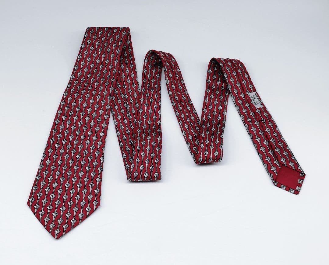 Red Hermes geometric H polyester necktie laid flat showing its full length and label on a white background.