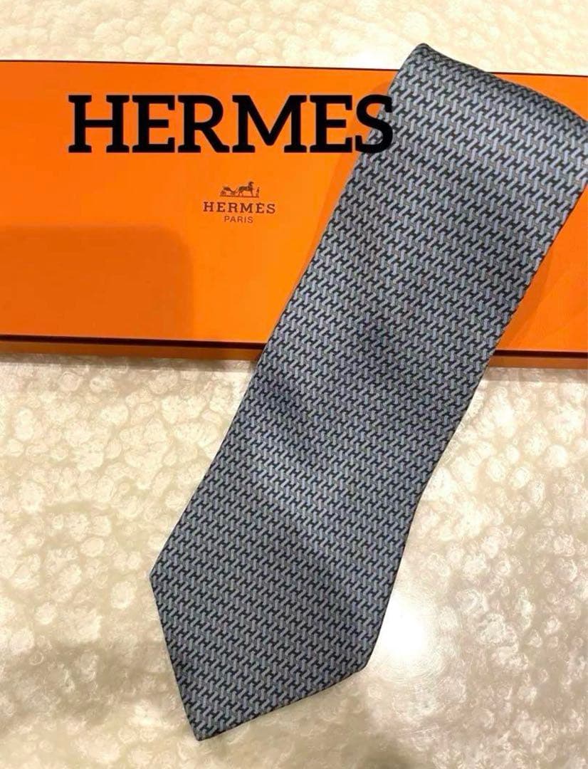 Blue-gray silk necktie with a small geometric pattern laid on an orange HERMES box.