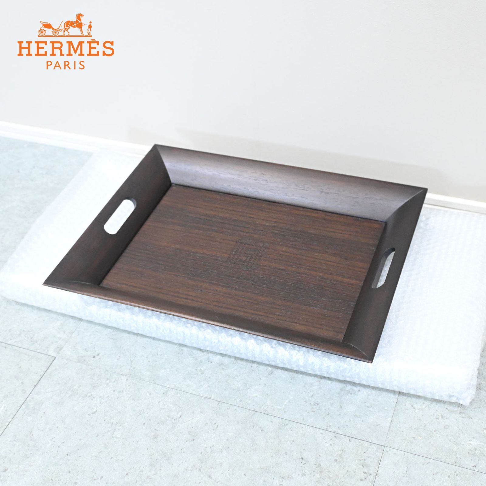 Dark brown wooden tray with raised sides and cutout handles shown on a white protective pad.