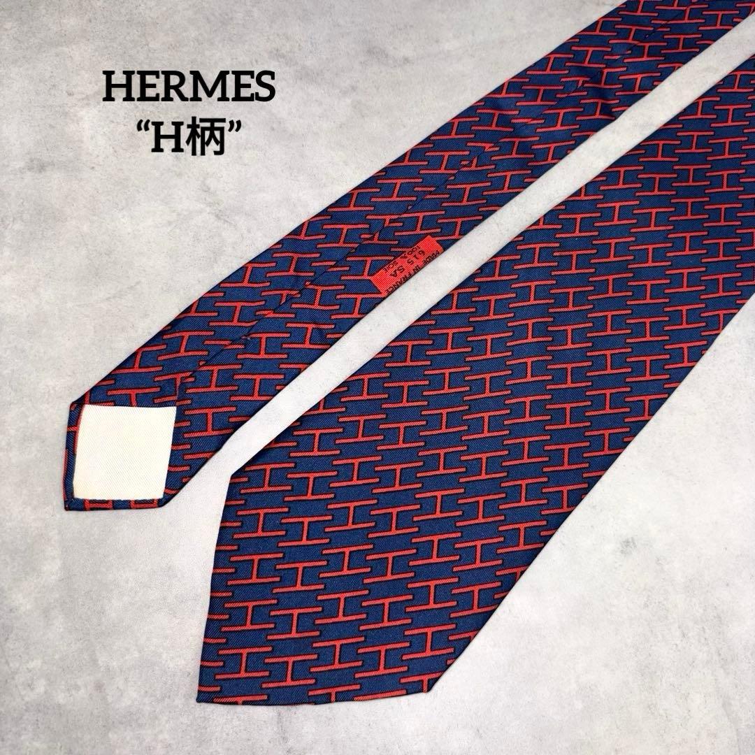 A navy and red patterned Hermes necktie with a repeating H-shaped motif laid flat on a light surface.