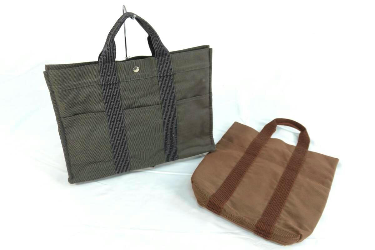 Two Hermes canvas tote bags (one gray with dark handles and one brown) on a white background.