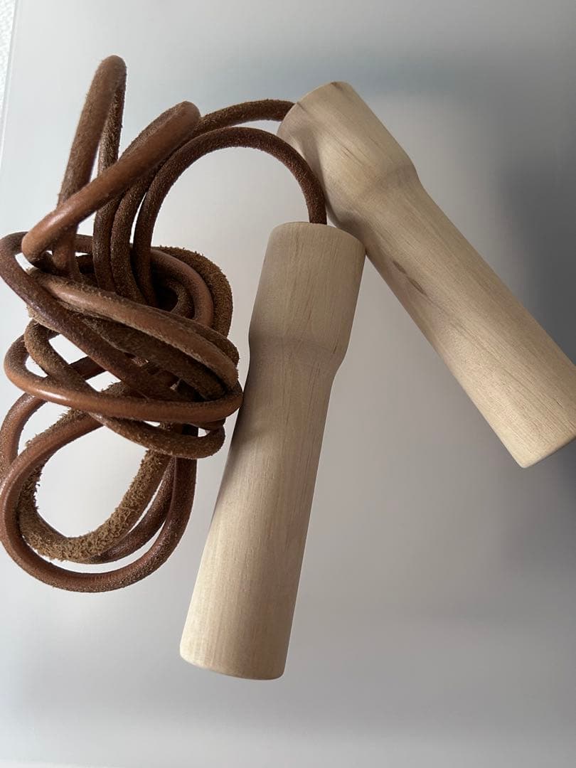 A jump rope with light wooden handles and a brown leather cord coiled beside them.