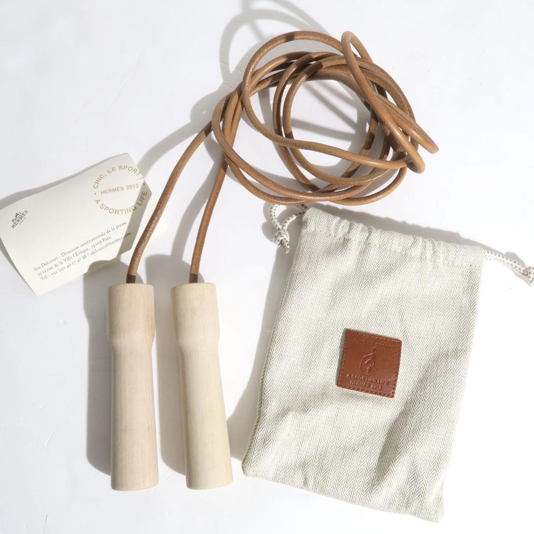 Hermes jump rope with two wooden handles, a coiled leather cord, and a small canvas drawstring pouch.