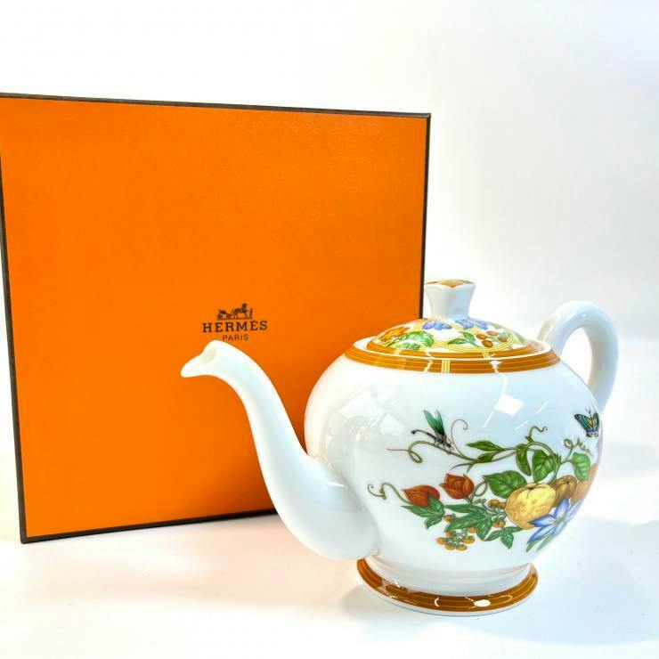 Hermès La Siesta white porcelain teapot with botanical fruit and butterfly pattern beside an orange Hermès box.