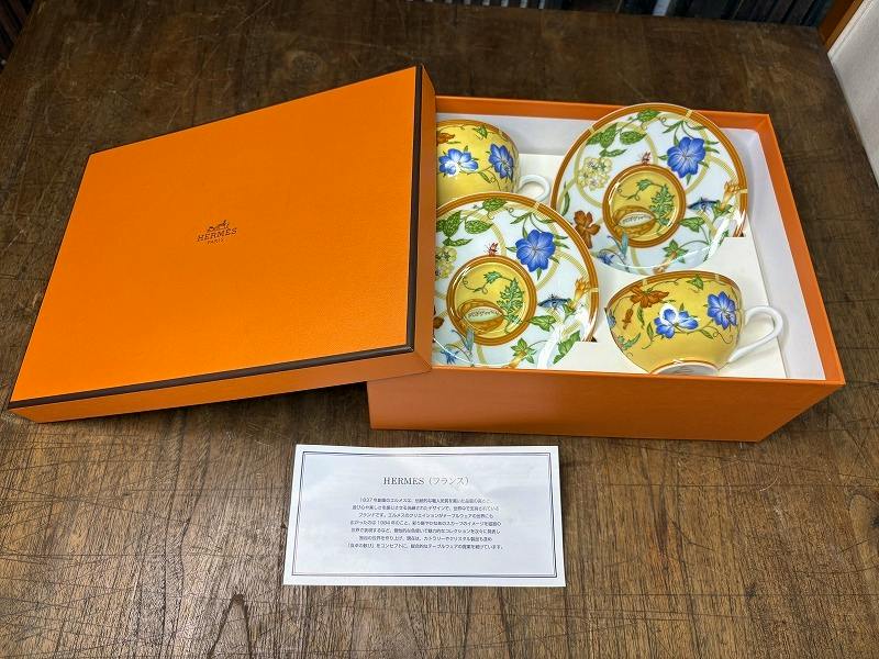 Two yellow Hermes La Siesta teacups with matching saucers displayed inside an open orange Hermes box with an information card.