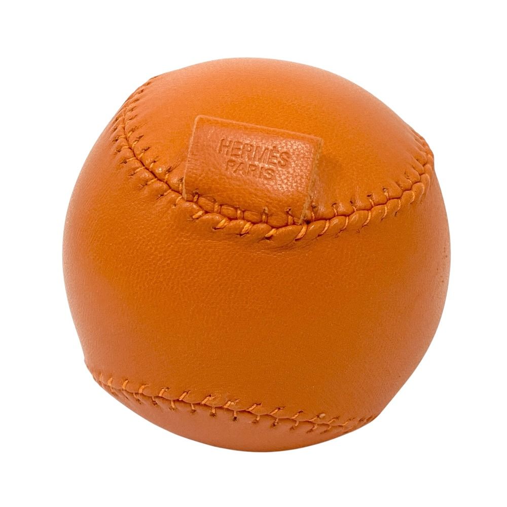 Orange leather baseball with visible stitching and an embossed HERMÈS Paris marking.