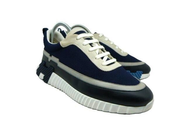 Pair of men’s HERMES sneakers in navy, white, and black shown at an angled front view.