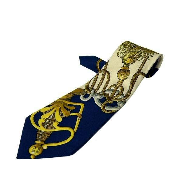 White and navy Hermes men's silk necktie with gold rope and tassel pattern on a white background.