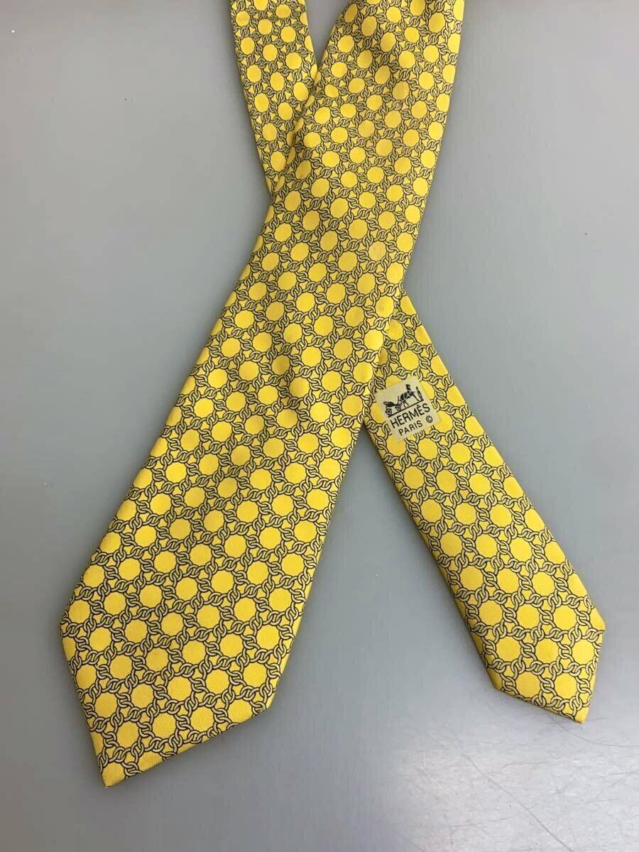 Yellow patterned Hermes silk necktie laid flat showing the Hermes Paris label on a gray background.