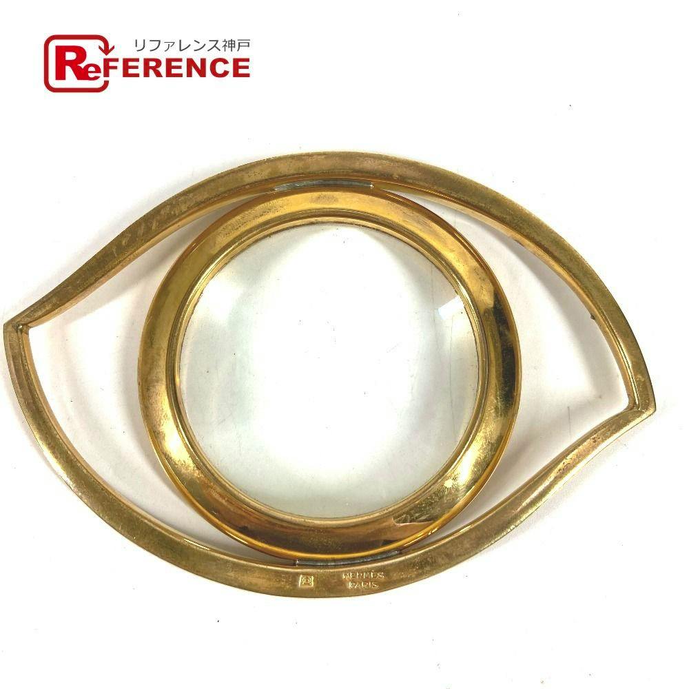 Gold metal loupe with a round magnifying lens in an eye-shaped frame on a white background.