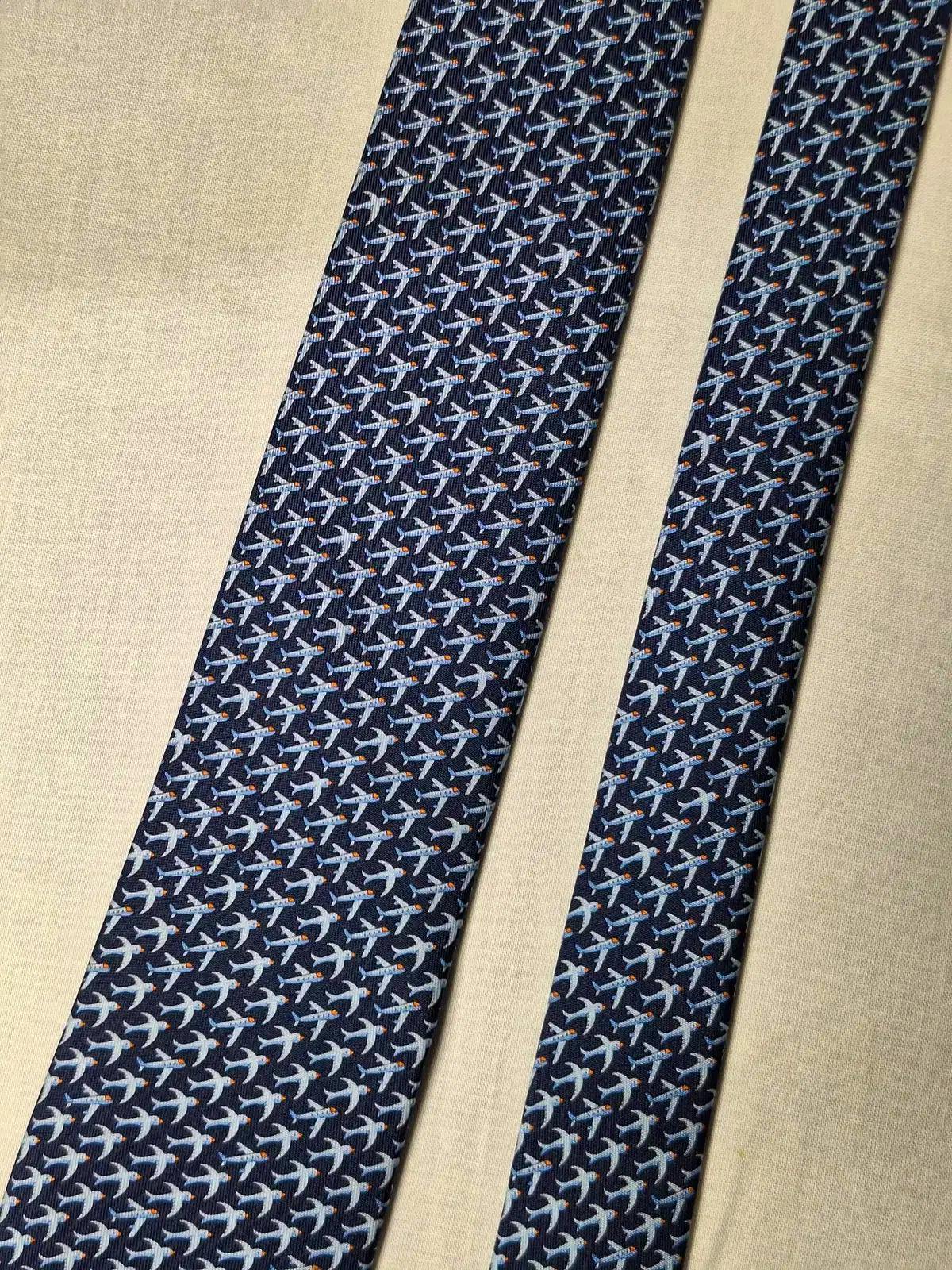 Navy necktie and its narrow end laid flat on a light surface, showing a repeating airplane pattern.