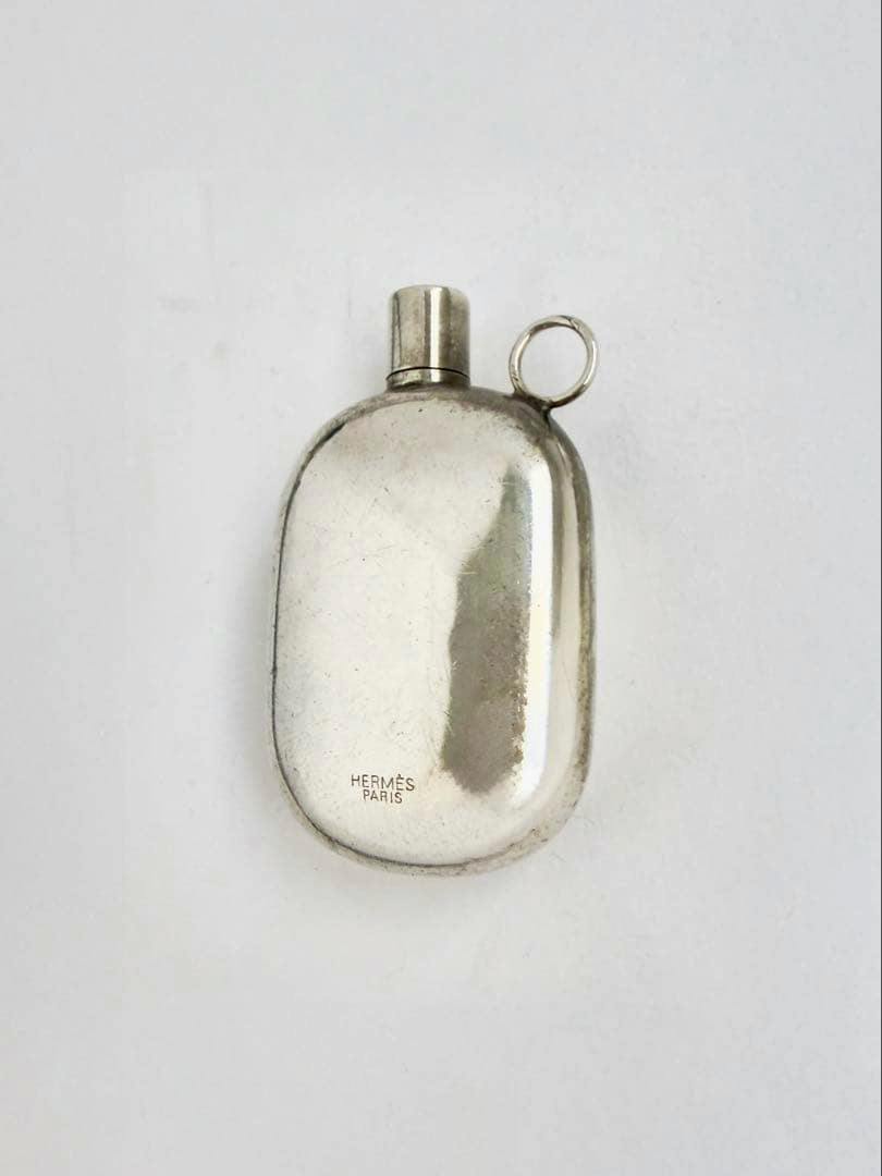 Silver HERMES perfume bottle pendant showing the HERMES PARIS engraving on a white background.