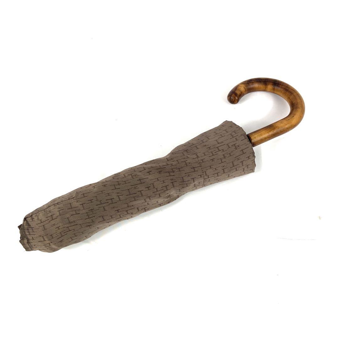 Closed HERMES folding umbrella (Parapluie pliant Pluie de H) with patterned brown fabric cover and a curved wooden handle on a white background.