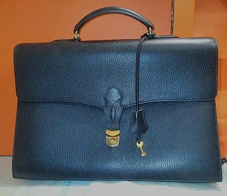Front view of a black Hermès cow leather briefcase with top handle and front flap lock.