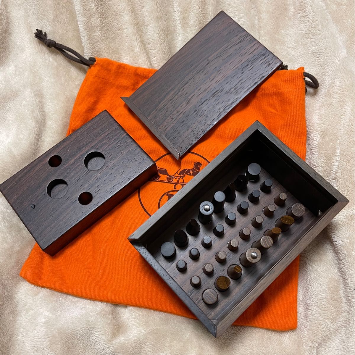 Open mahogany wooden chess game box showing wooden pieces and two lids displayed on an orange Hermès dust bag.