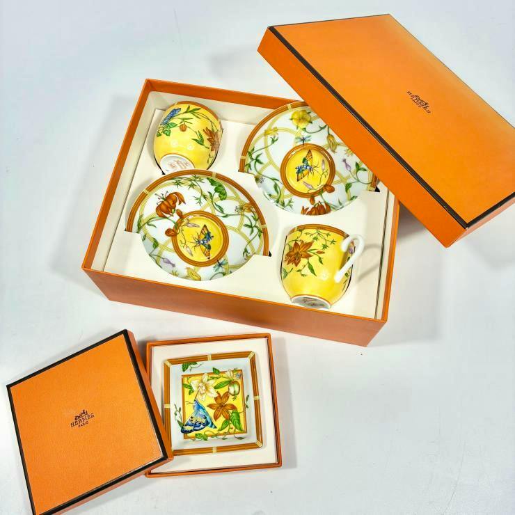 Hermès Siesta floral-patterned tea cups and saucers with a square mini plate arranged inside an open orange Hermès box.