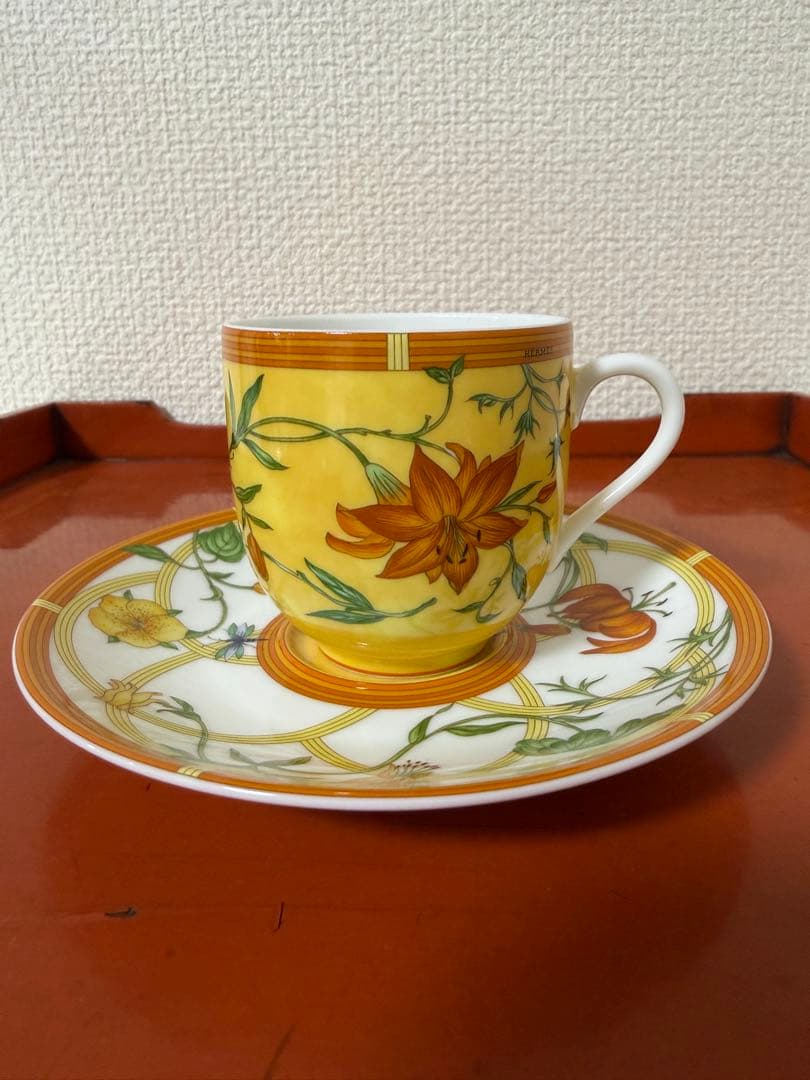 Demitasse porcelain cup and saucer with a yellow floral pattern pictured on a wooden tray against a textured wall.