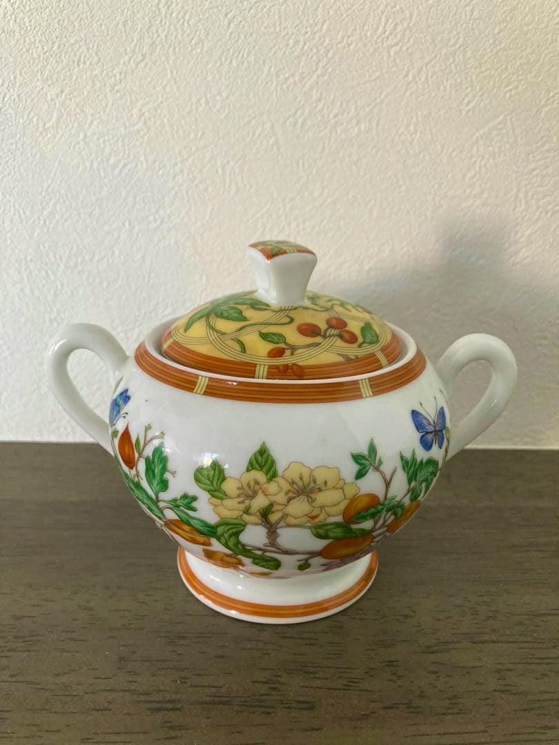 White porcelain Hermès Siesta sugar pot with floral and butterfly decoration and lid, photographed on a wooden surface.