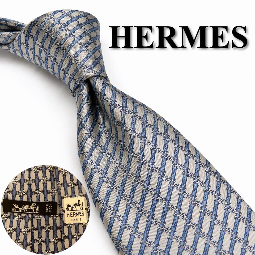Hermes necktie in blue and white with a repeating chain/H pattern shown knotted, with a small inset showing the label.