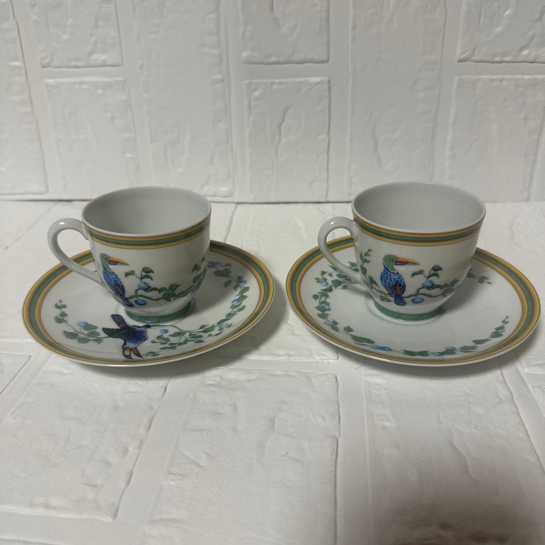 Two porcelain demitasse cups with matching saucers featuring a toucan and foliage pattern on a white background.